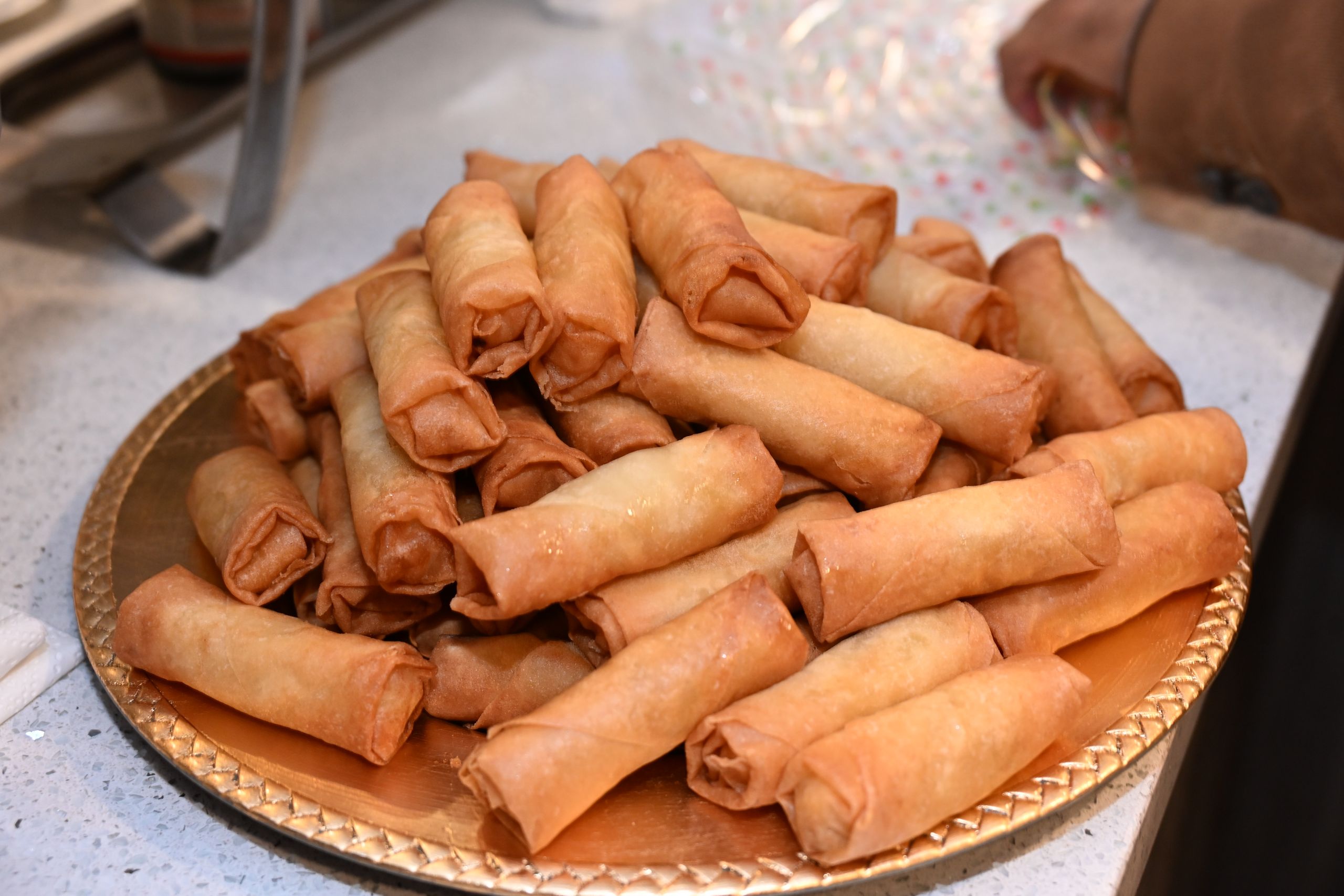 A heap of golden, crispy spring rolls displayed on a decorative tray, ready to serve.